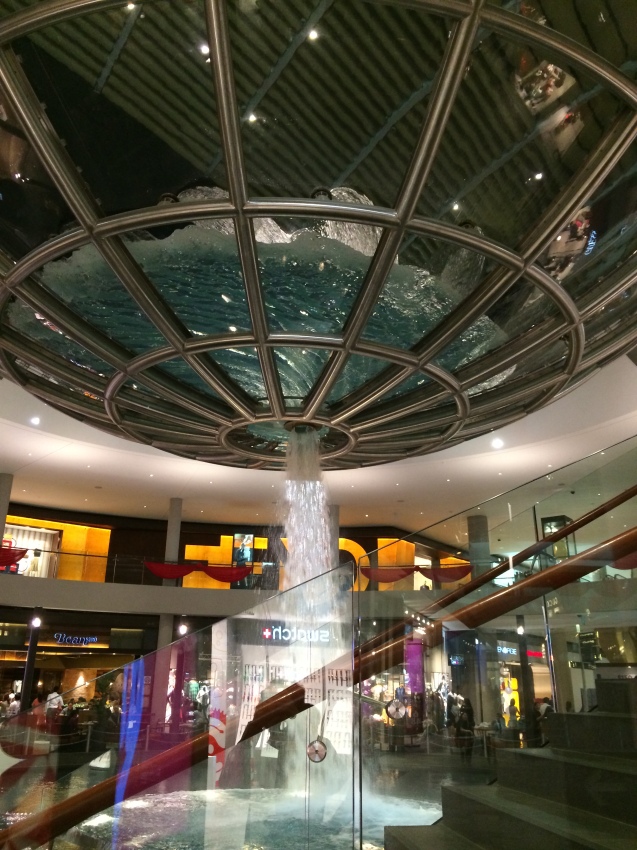 Water art in the Shoppes at Marina Bay Sands. Water gushes from the room, flowing in a circular pattern from the glass bowl above.